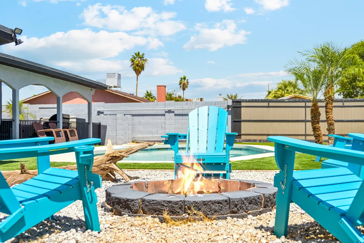 An exterior shot showcasing a swimming pool, turquoise chairs for lounging, and a fire pit area. The scene invites both solo relaxation and social gatherings, with a backdrop that encourages outdoor activity and connection to the local environment.