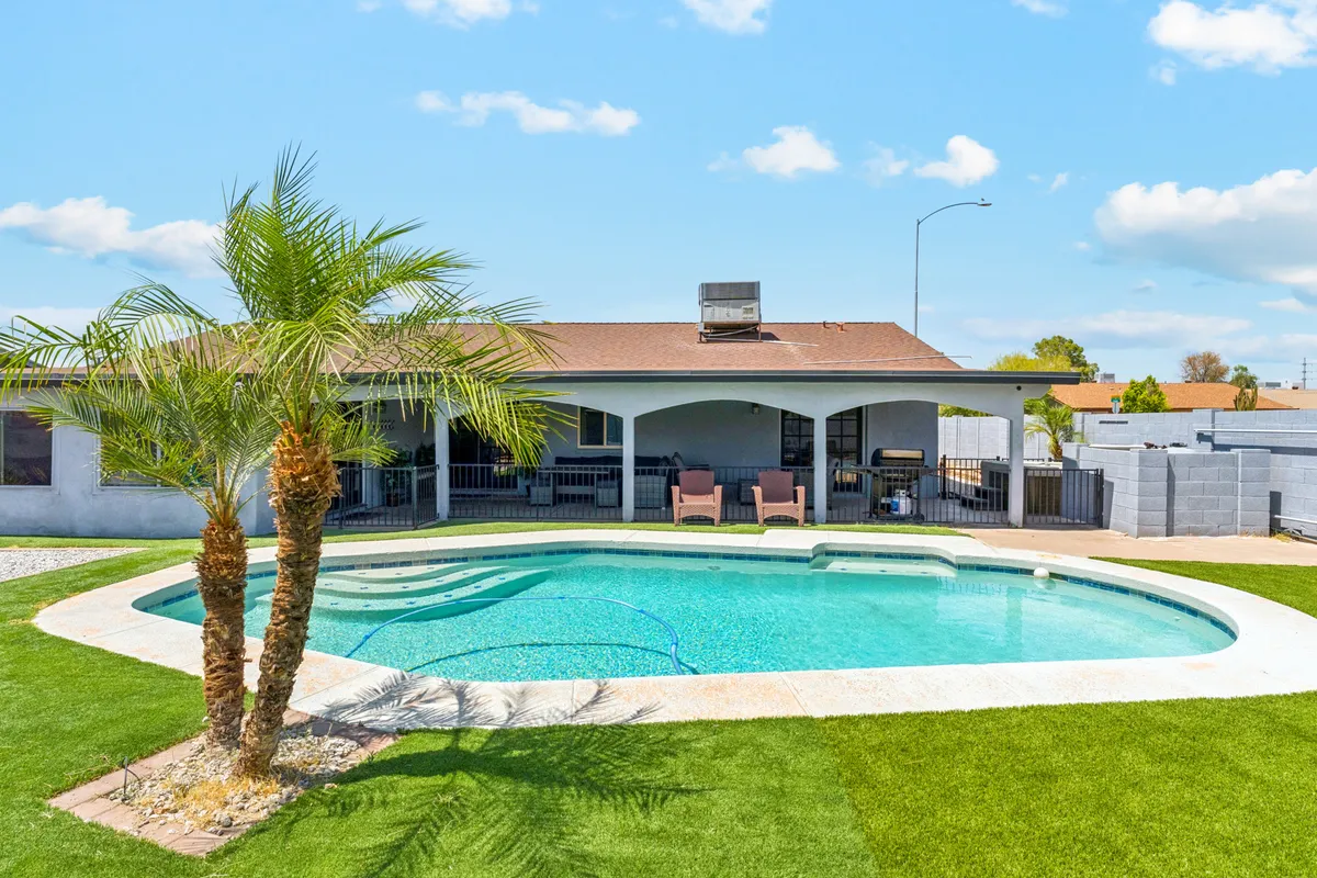A sparkling swimming pool surrounded by palm trees, with patio seating arranged for relaxation. The space feels sunny and inviting, with plenty of lounge chairs perfect for sunbathing or keeping an eye on children while they swim. The pool is clearly the focal point, emphasizing the home's private outdoor recreation area.