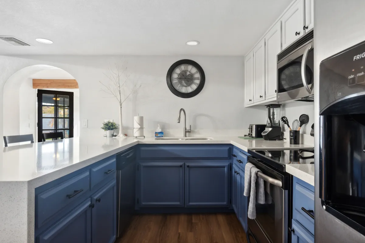 A fresh, modern kitchen featuring blue cabinetry, white countertops, modern appliances, and a decorative wall clock. The space is bright, organized, and ideal for both cooking and entertaining.