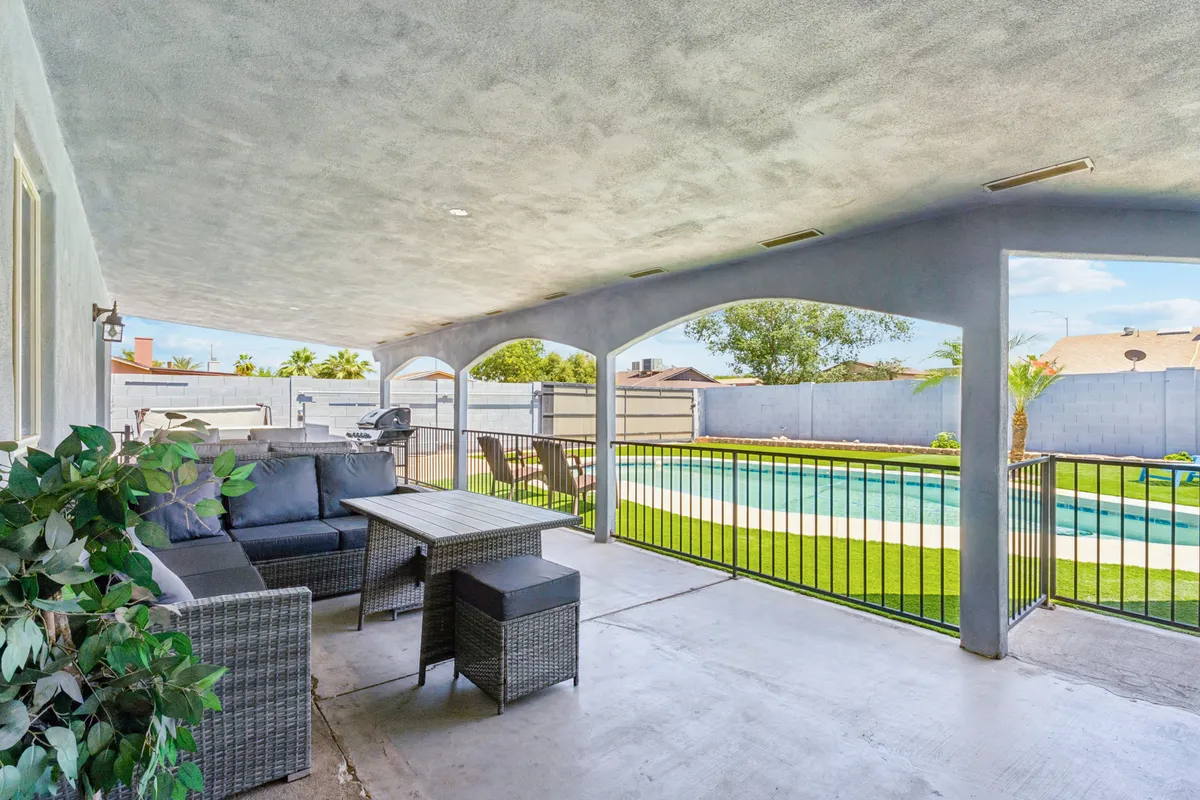 A vibrant backyard scene featuring an outdoor seating area overlooking a sparkling swimming pool, framed by a lush green lawn and decorative plants. The setup evokes a sense of relaxation and entertainment, perfect for family gatherings or sunset soirees.