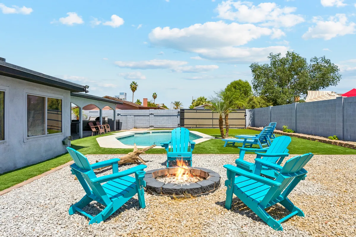 A cheerful backyard scene with a fire pit, Adirondack chairs, landscaped garden, and swimming pool. The setup is ideal for both day and evening gatherings, allowing for swimming, socializing, and relaxing by the fire under the stars.