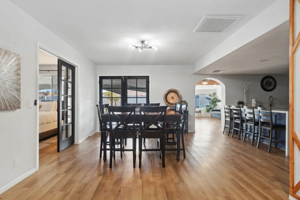 A spacious, sunlit dining area with a dining table set for guests, black French doors opening to the outside, and an open view into the kitchen area. The space features contemporary finishes and feels both inviting and lively, ideal for hosting family meals and social gatherings.