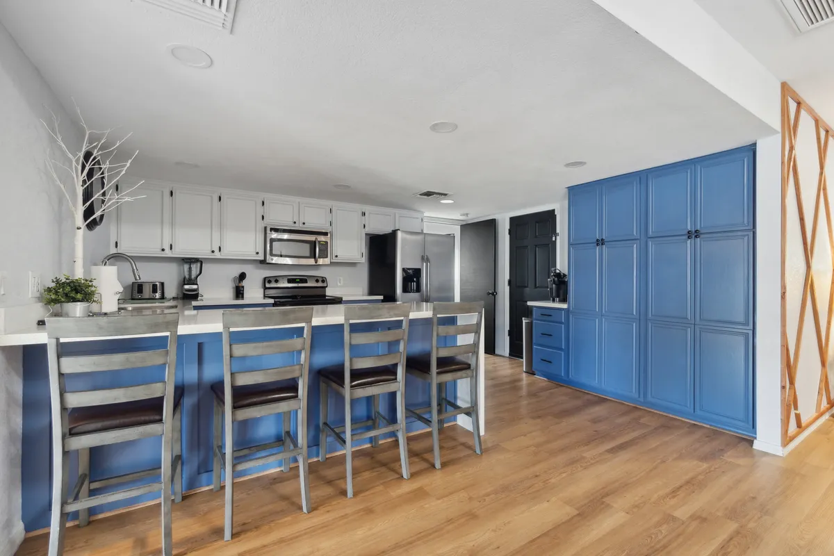 A modern kitchen scene focused on blue cabinetry, stainless steel appliances, and a breakfast bar with comfortable seating. The design is cohesive, stylish, and welcoming, promoting both meal preparation and casual dining.
