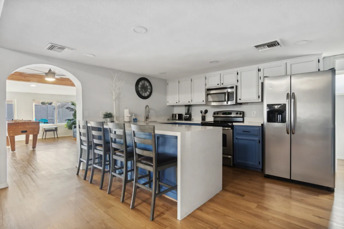 A bright, spacious kitchen featuring a prominent kitchen island with bar stools, gleaming stainless steel appliances, and striking blue cabinetry. The layout is open, inviting interaction between the chef and guests. Ample counter space and modern fixtures create a highly functional and stylish cooking environment.