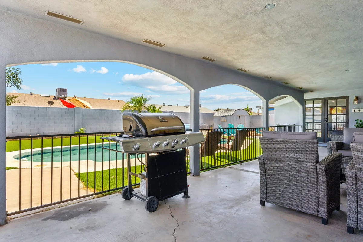A backyard scene with a pool, outdoor grill, and comfortable seating. The area is designed for barbecues, socializing, and relaxing poolside—ideal for family time or entertaining friends, all set against the backdrop of Arizona's sunny weather.