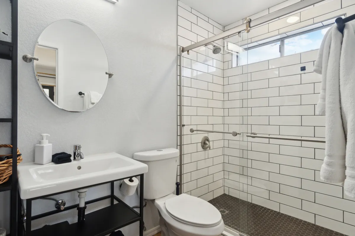 A bright, modern poolside bathroom with a large mirror, glass shower enclosure, sink, and towel rack. The space feels fresh and inviting, ideal for guests to shower or refresh after a swim without going indoors.