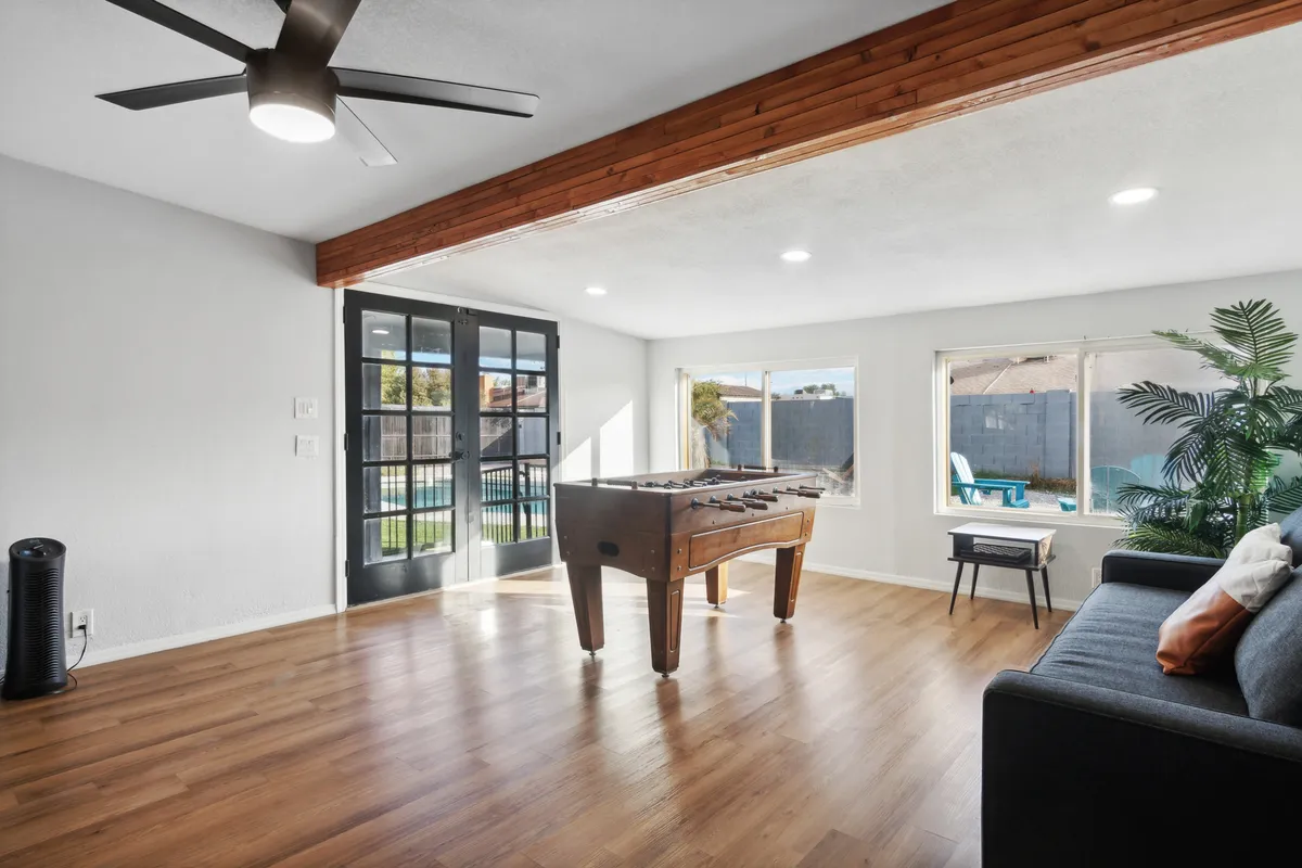 A playful, welcoming living area featuring a foosball table, large windows allowing in ample natural light, a cozy sofa, and potted plants. This area is ideal for game nights and casual relaxation, supporting interaction and memory-making.
